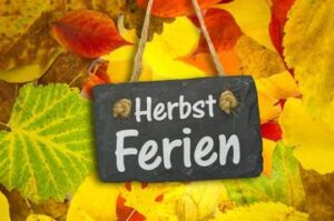 Schild mit Aufschrift "Herbstferien"; Blätter im Hintergrund